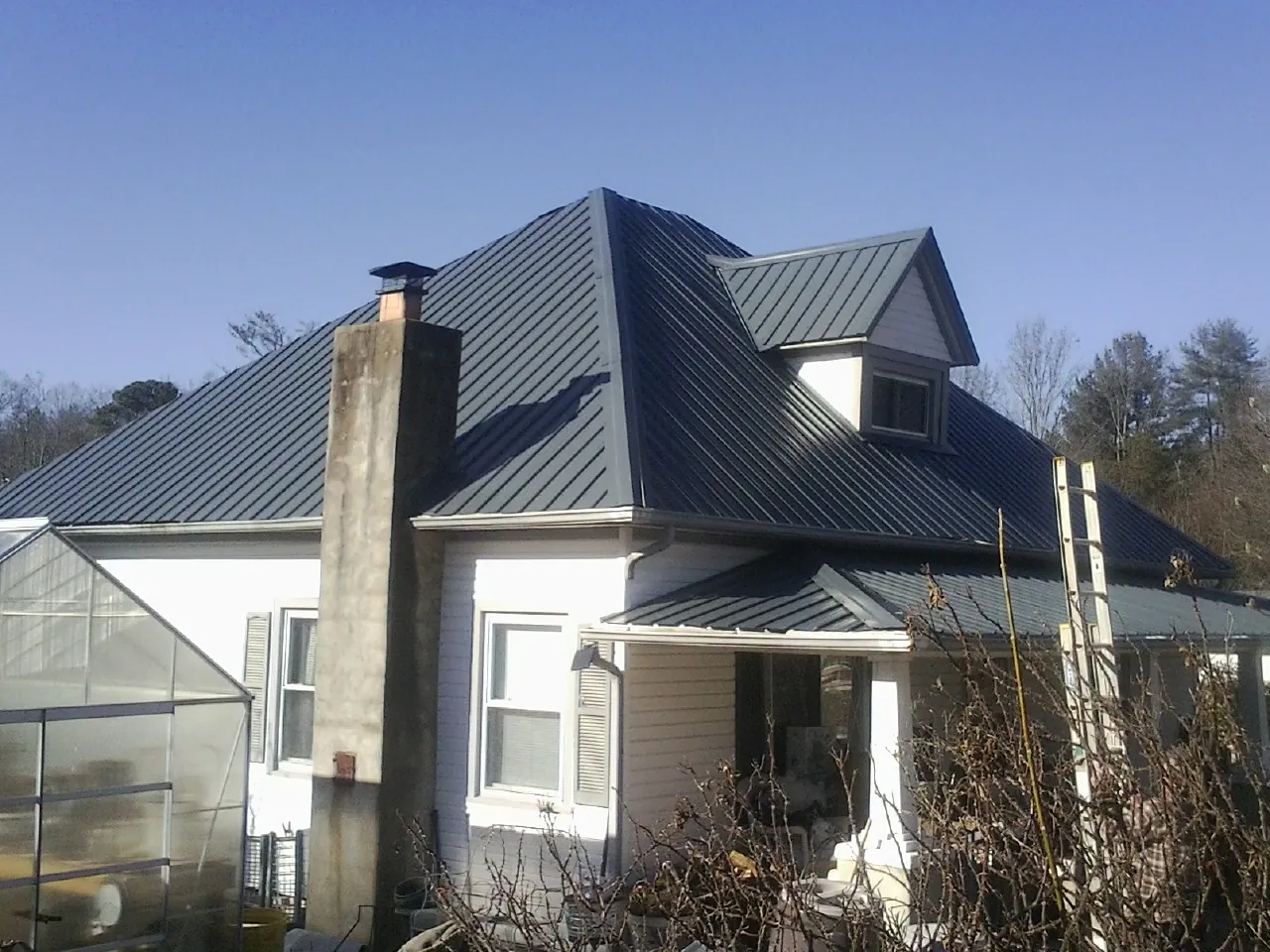 Dark blue standing seam metal roof on a white farmhouse with dormer in Attica