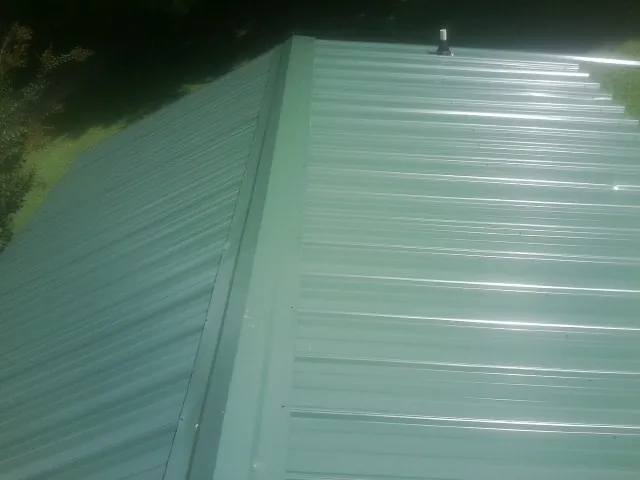 New green metal panels meeting at the ridge of a roof — Flat Roof Repair work by our crew in Attica